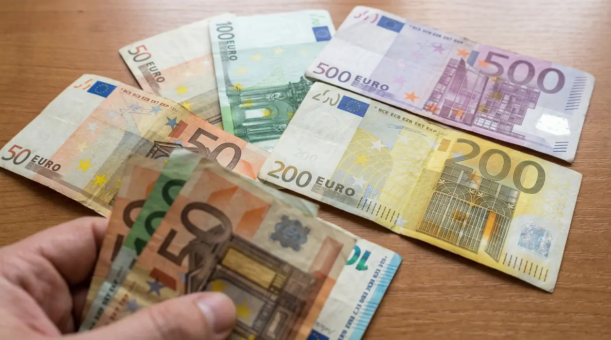 Banconote in euro di diversi tagli su un tavolo con una mano che le tiene