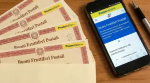 Buoni fruttiferi postali accanto a uno smartphone con sito di Poste Italiane aperto