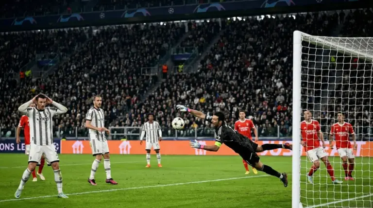 Un portiere in tuffo tenta di parare un tiro durante Juventus-Benfica, con giocatori e pubblico sullo sfondo