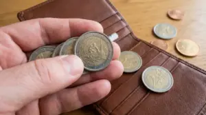 Una mano tiene alcune monete da 2 euro vicino a un portafoglio marrone aperto su un tavolo