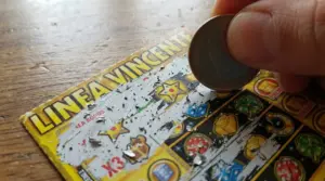 Una mano gratta un biglietto gratta e vinci usando una moneta su un tavolo in legno