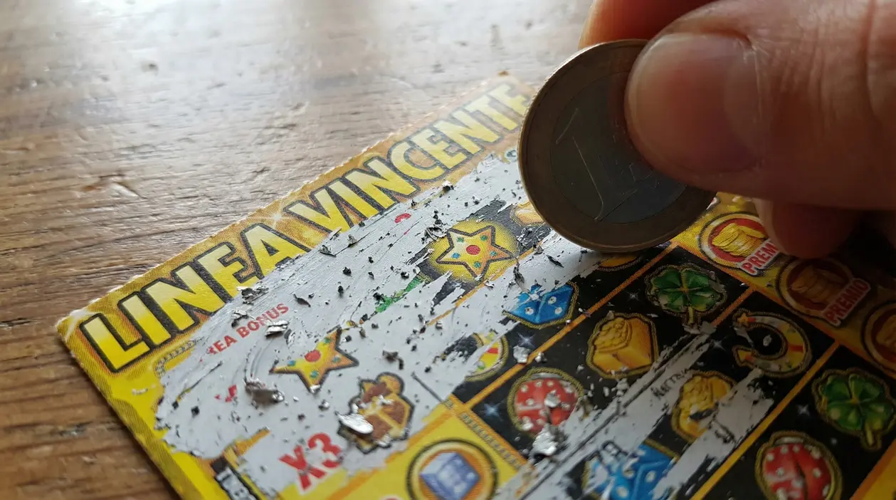 Una mano gratta un biglietto gratta e vinci usando una moneta su un tavolo in legno