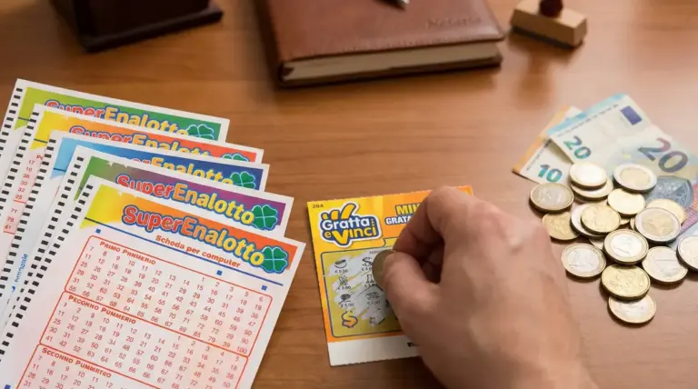 Mano che gratta un biglietto 'Gratta e Vinci' vicino a schedine del Superenalotto e soldi in euro