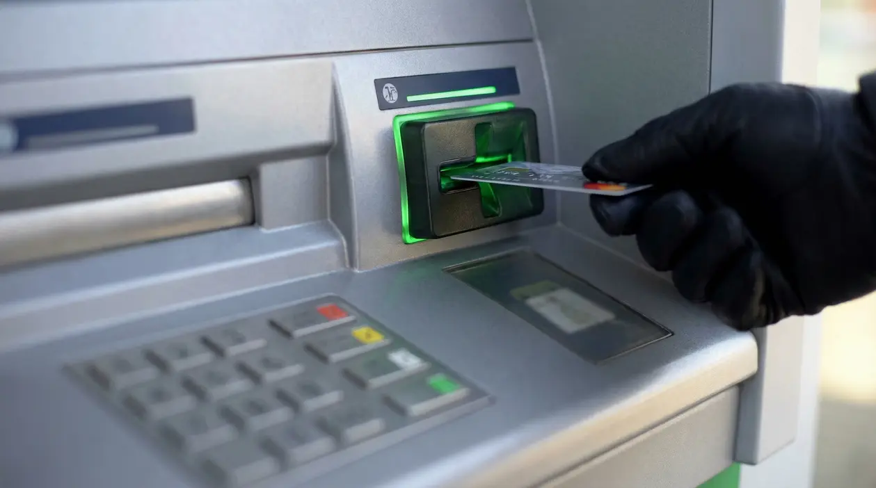 Una mano con guanto inserisce una carta in uno sportello bancomat