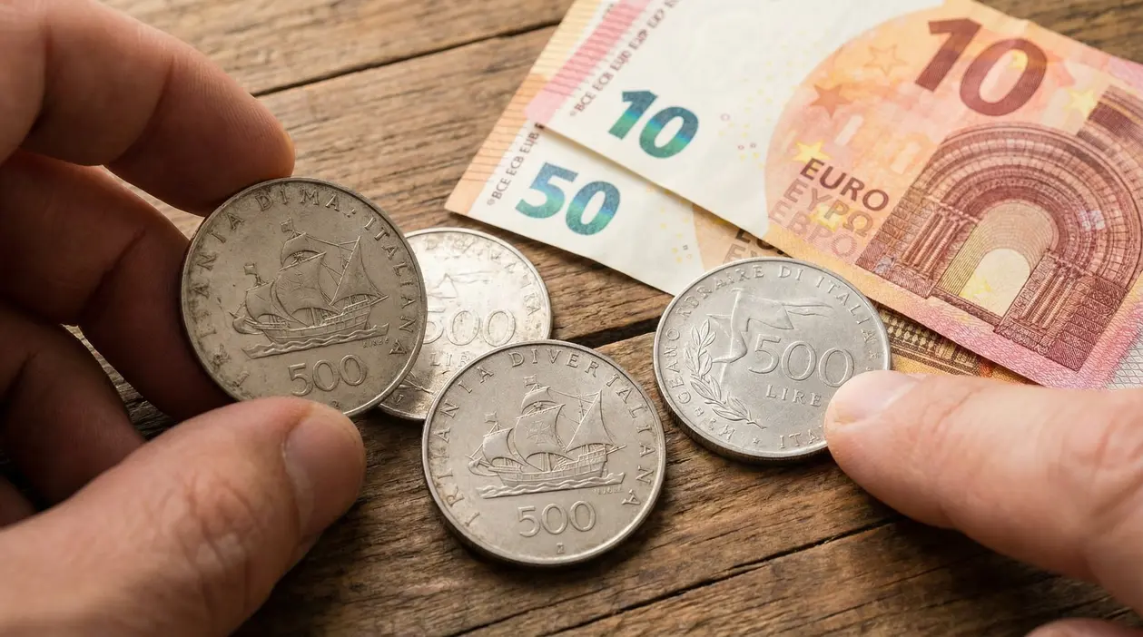 Monete da 500 lire d'argento accanto a banconote in euro su tavolo di legno