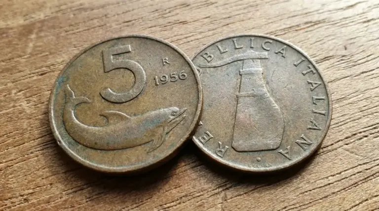 Due vecchie monete italiane da 5 lire con un delfino e un timone su sfondo di legno