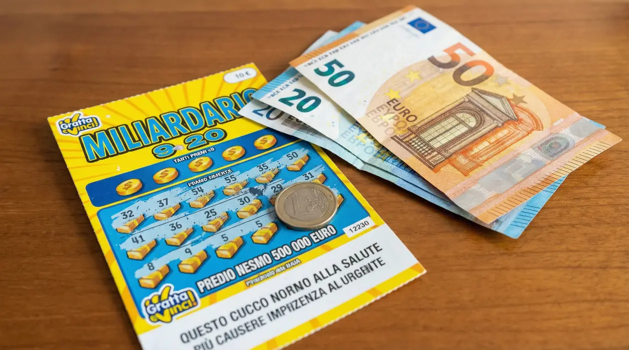 Biglietto del Gratta e Vinci con monete e banconote da euro su un tavolo in legno