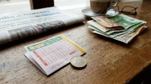 Schedina del Superenalotto con una moneta da un euro su un tavolo, accanto a banconote